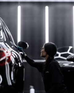 A professional technician conducting a final inspection and surface wipe down on a black car before ceramic coating application.
